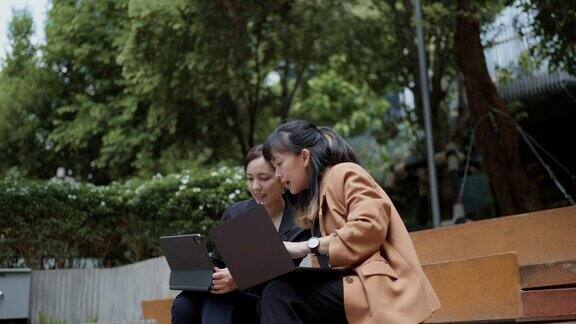 亚洲女商人坐在现代办公空间的花园里一边用笔记本电脑一边聊天