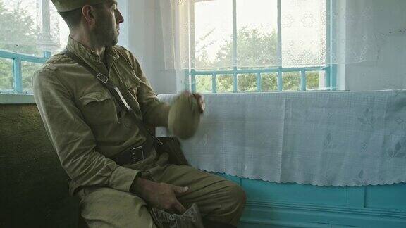 退伍士兵在老房子里休息在二战期间成年苏联士兵坐在老房子里的桌子旁从袋子里取出瓶子从窗户往外看