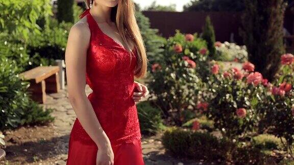 可爱的女孩穿着红色长裙头上戴着皇冠在花园里与玫瑰摆姿势