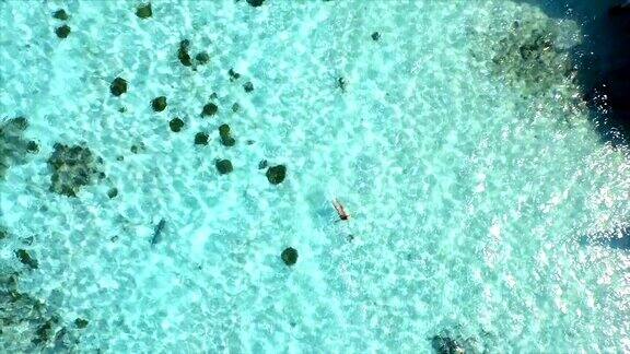 空中慢镜头:美丽的年轻女子游泳躺在清澈的海面上