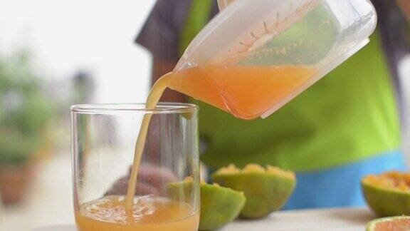 家庭主妇在家准备早餐的时候手里正在挤橙汁倒进杯子里自制的