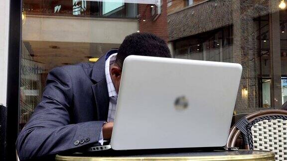 年轻疲惫的商人坐在咖啡馆里用笔记本电脑工作:劳累过度