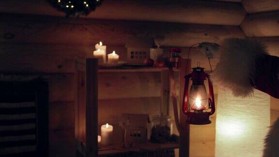 圣诞老人手里拿着一盏油灯在装饰精美、点着蜡烛的木屋里来到圣诞树前