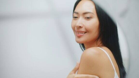美丽的亚洲女人触摸她的完美柔软的肩膀脖子在镜子里性感的微笑快乐的女性享受她的美丽健康天然化妆品护肤品聚焦肖像