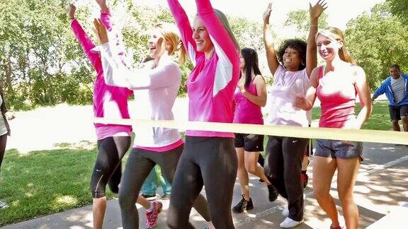 大型团队的妇女越过终点线在乳腺癌意识的慈善比赛