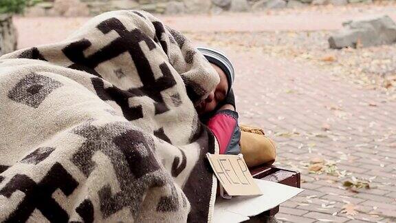 一个深思熟虑的流浪汉躺在公园的长椅上举着“帮助”的牌子乞讨贫穷