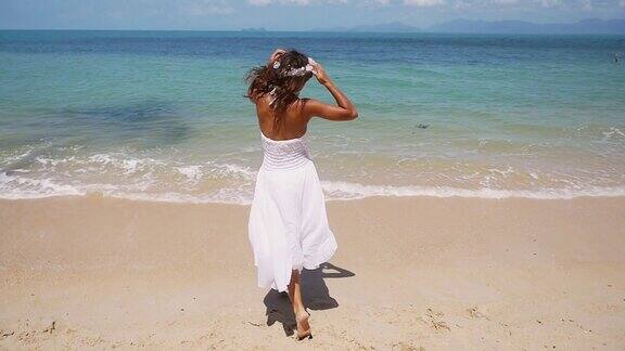 快乐的年轻女子穿着白色的衣服戴着花环赤脚跑向大海高兴地举起双手白色沙滩1920x1080慢动作高清