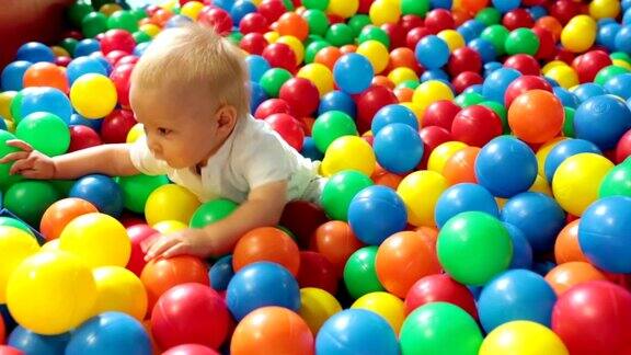 可爱的蹒跚学步的小男孩在室内的儿童操场上玩五颜六色的球