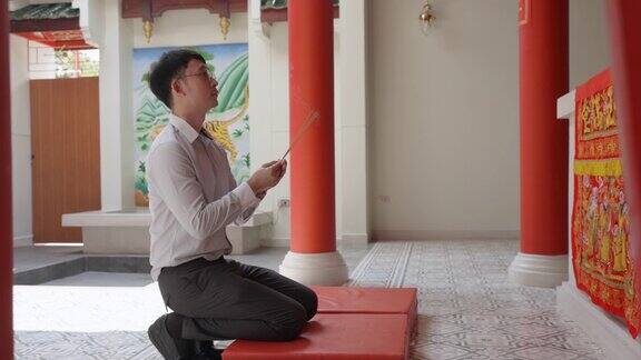 一名亚洲男子在中国神祠里跪着举着香柱祈祷