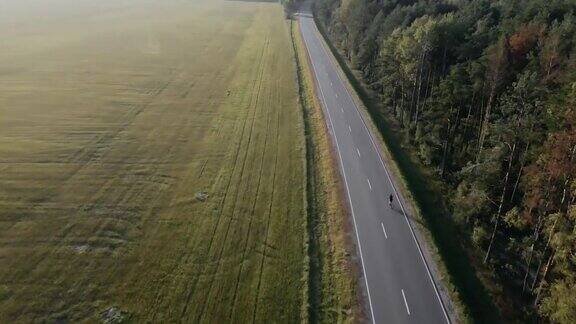 航拍视频骑自行车的人骑公路自行车在公路附近的田野在夏天