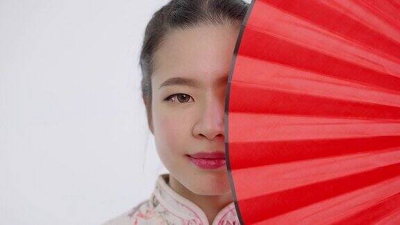 近景中国亚洲美丽的女子在春节穿着旗袍白色花卉图案的衣服红色的扇子盖住她的左半边脸看着镜头
