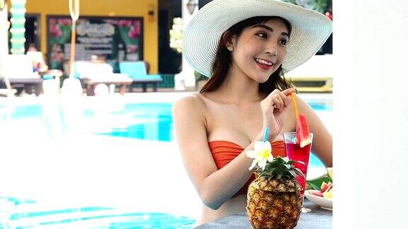 夏天性感的亚洲女人在橙色比基尼与热带饮料在游泳池