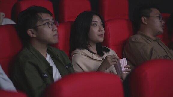 亚洲华裔年轻夫妇一起吃着爆米花在电影院看电影