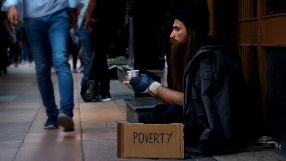 无家可归的人拿着“贫穷”纸板在拥挤的街道上乞讨