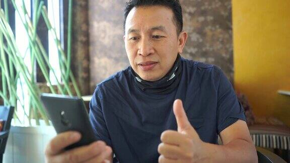 成熟的亚洲男人在咖啡店使用手机好迹象竖起大拇指