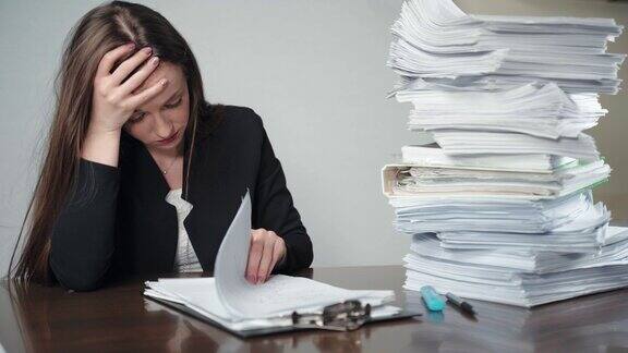 办公室办公桌上堆放着一堆未完成的文件和文件压力和疲惫的女办公室会计坐在文件前握着她的头与手紧张的工作人员有头痛和不知所措的财务
