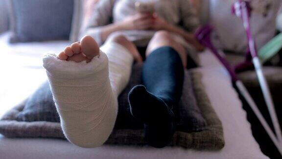 腿部骨折的残疾妇女和石膏足在家使用智能手机