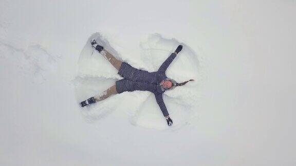 无忧无虑的年轻女子挥舞着她的手臂和腿在雪堆天使