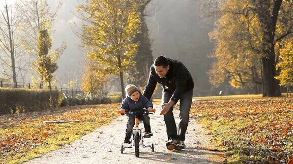 父亲带着孩子在秋天公园里骑自行车