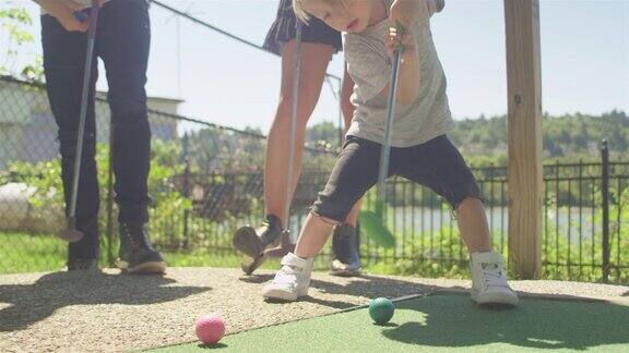 一个小孩在高尔夫球场上奋力击球他走出镜头终于击中了球把他的高尔夫球杆扔了出去
