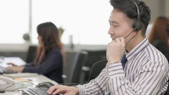 亚洲男子电话营销操作员戴着耳机与团队工作在呼叫中心城市办公室