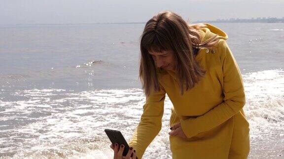 一名快乐的年轻女子在海滩上用手机自拍并在社交媒体上发布