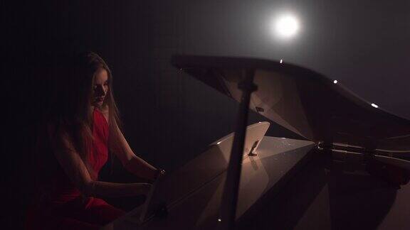4K镜头的女钢琴家在音乐会的舞台上演奏美丽的大钢琴一个女人在音乐厅里弹钢琴舞台灯光和背景光雾