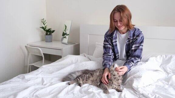 穿着睡衣的漂亮女孩亲吻一只灰色的小猫一个年轻的女人抱着一只坐在床上的猫
