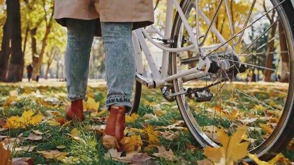 在秋天城市公园不知名的女人走着自行车的腿跟踪镜头慢动作后视图关闭