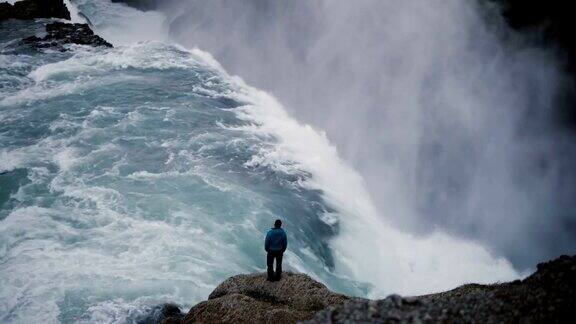 男人站在悬崖瀑布边欣赏壮阔的美景