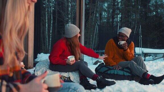 开朗快乐的多民族朋友饮茶、谈笑风生坐在懒人沙发上惬意的冬屋阳台慢动作