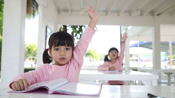 一个女学生举手回答老师的问题两个女孩坐在桌子旁一个学生举手回答老师的问题
