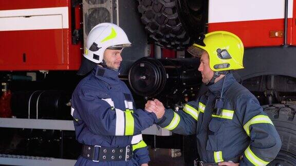 两名身穿防护服、头戴头盔的消防员与消防车亲切握手