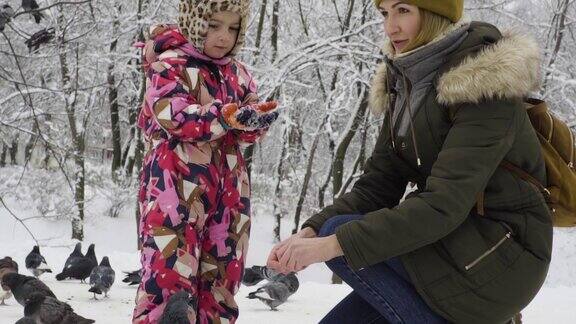 妈妈和女儿在一个冬季公园里喂鸽子