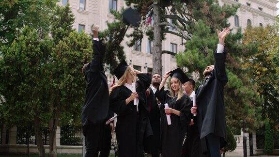 多民族的毕业生们毕业后在大学公园里非常兴奋地举起毕业帽手里拿着毕业证