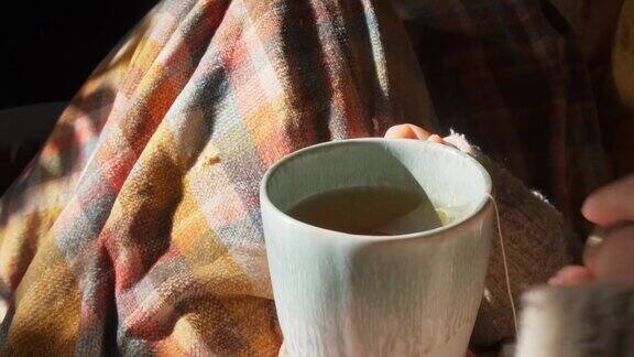 一个女人的手在一个舒适的室内环境与格子花呢喝热花草茶的特写