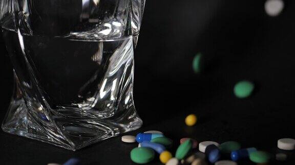 药店的主题彩色孤立药丸胶囊在黑色表面靠近水玻璃维生素落在暗色的表面一堆五颜六色的圆形胶囊带着药抗生素