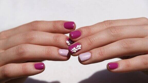 女人的手与紫色和粉红色的指甲设计在白色的背景