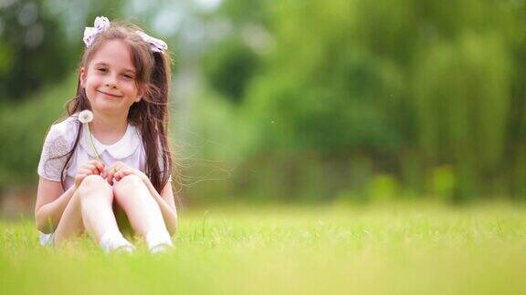 可爱微笑的女孩在绿色的草地上有趣快乐的女孩带着花的肖像坐在绿色的草地上