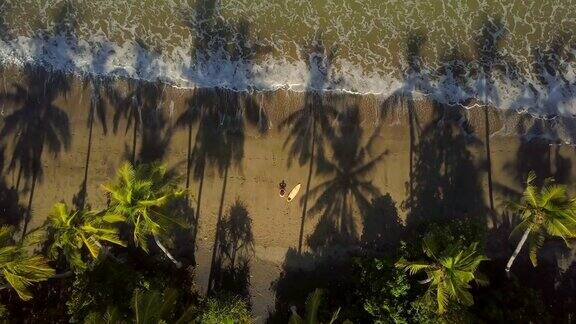 航拍:冲浪运动员坐在美丽的热带海滩上看着镜头