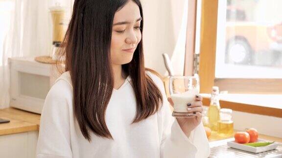 年轻的亚洲女人在厨房里喝牛奶