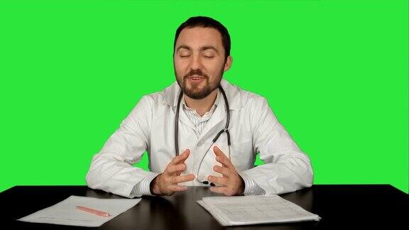 笑容开朗的医生在绿色屏幕上看着摄像头带着好消息色度键