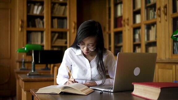 勤奋的女学生生物学家在桌子上写书和笔记本电脑在图书馆