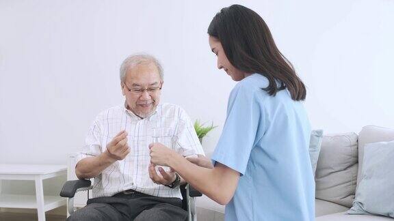 一个亚洲老人拿着一个药丸胶囊和一杯由他的照顾者准备的饭后服用的水