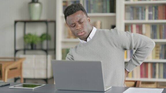 非洲男子在图书馆使用笔记本电脑时背部疼痛