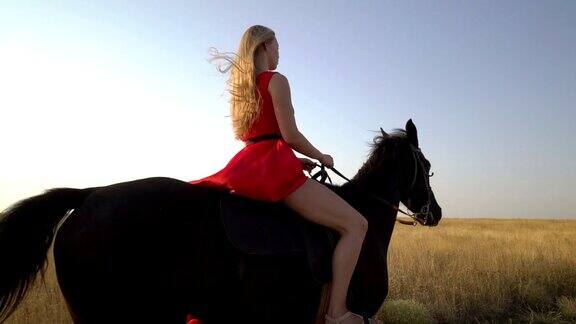 年轻的金发姑娘骑着马穿着红衣服在乡间小路上骑马