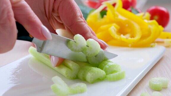 女性用手用刀将芹菜茎切成小片金属刀在厨房餐桌上的灰色塑料板上切芹菜厨师用生的健康蔬菜做素食沙拉