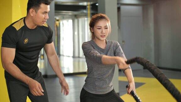 亚洲女人与私人教练在健身房与战斗绳