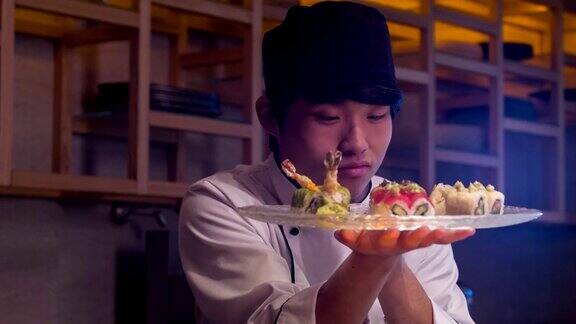 微笑的亚洲厨师在白色制服站在厨房的寿司吧旋转盘与卷