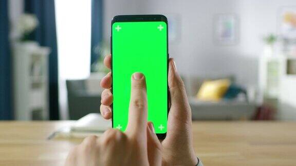 一个男人的特写持有绿色模拟屏幕智能手机和使用触摸屏手势触摸手机色度键屏幕在背景舒适的家庭气氛